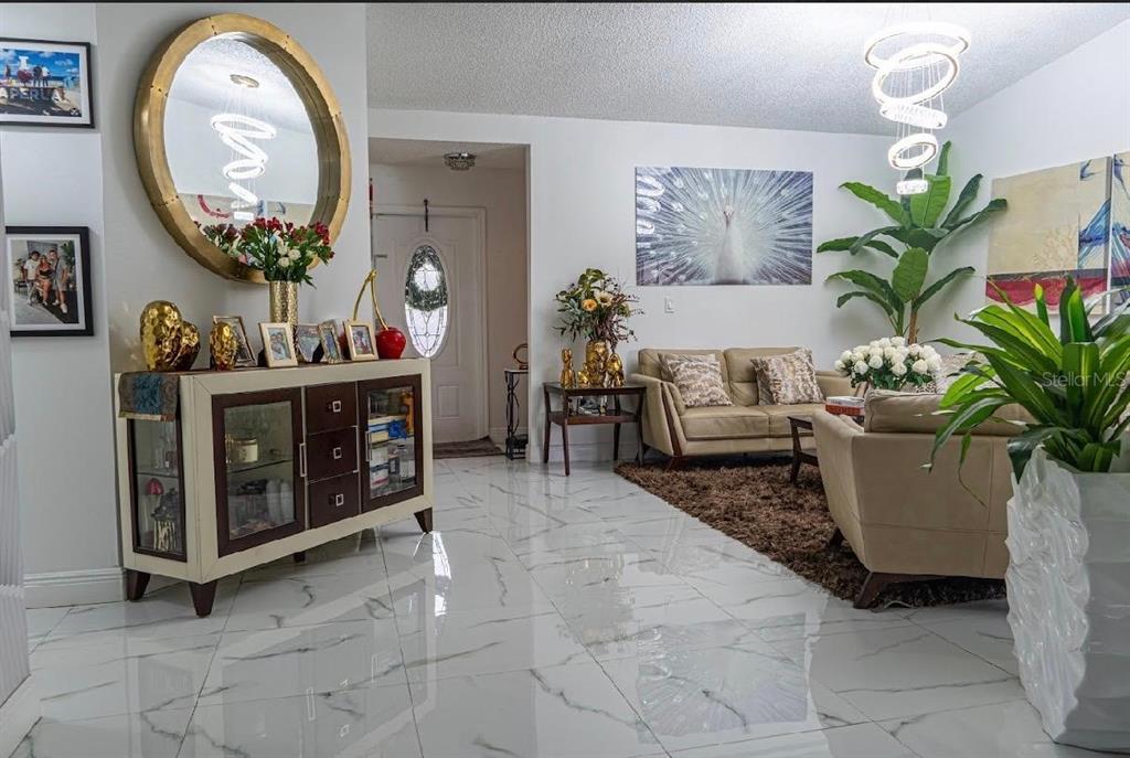 A living room features white marble floors, a gold-framed mirror, and a modern chandelier — 8419 NW 193RD LN, HIALEAH, FL