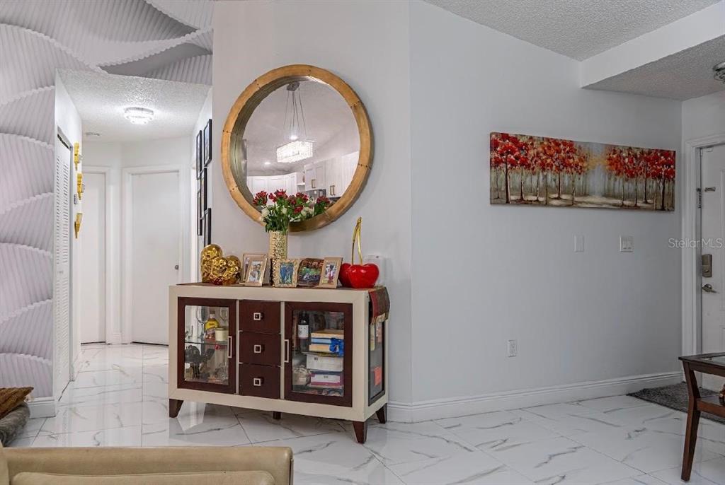 A white-tiled entryway features a wooden sideboard, a large round mirror, and wall art — 8419 NW 193RD LN, HIALEAH, FL