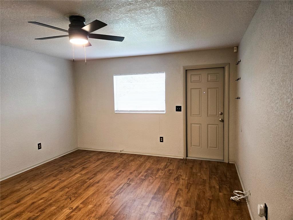 An empty room features wood-look flooring, a ceiling fan, a window with blinds, and a door — 1517 S TAYLOR ROAD, SEFFNER, FL