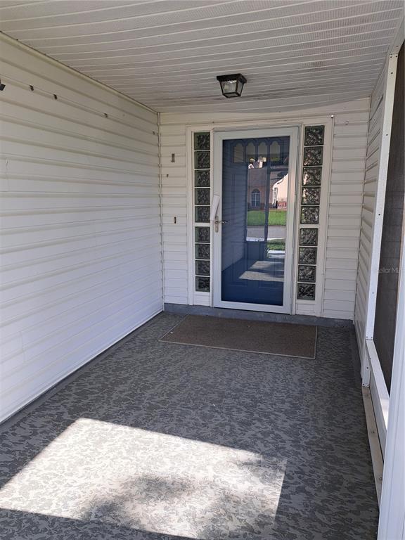 A covered front porch features white vinyl siding, a glass storm door, and decorative glass blocks — 5618 ROSEWALL CIRCLE, LEESBURG, FL