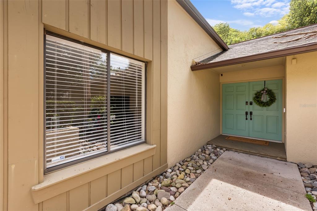 A light-colored house exterior features a large window with blinds and a teal double door — 956 STONEWOOD LANE, MAITLAND, FL