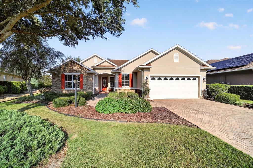 A single-story suburban house with a tan stucco exterior, stone accents, and a paved driveway — 8943 SW 86TH LOOP, OCALA, FL