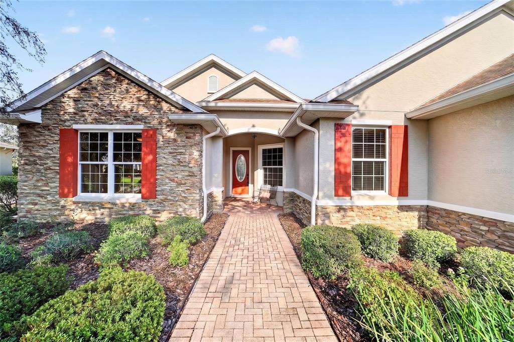 A covered porch features a red front door, a large window, and a metal bench — 8943 SW 86TH LOOP, OCALA, FL