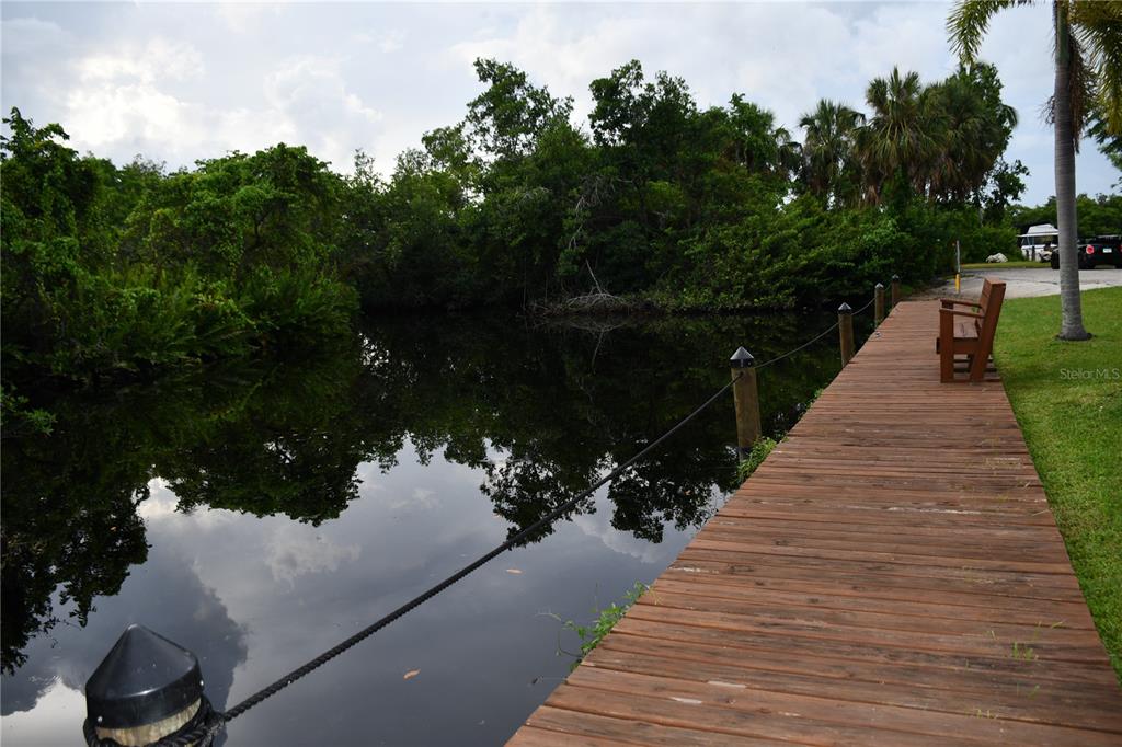 A wooden dock with a bench extends over a dark canal bordered by dense trees — 1591 SUNKIST WAY, FORT MYERS, FL