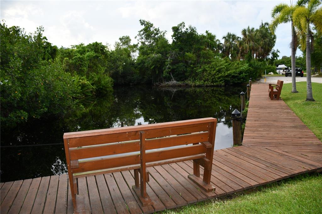 A wooden dock with two benches extends over a dark pond surrounded by lush trees — 1591 SUNKIST WAY, FORT MYERS, FL