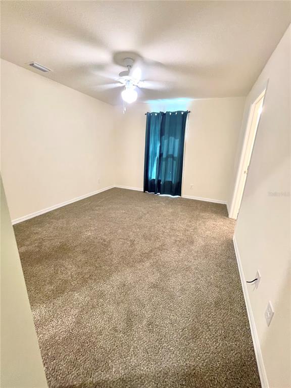 An empty bedroom features beige carpet, off-white walls, a ceiling fan, and a teal curtain — 5029 W HUMMINGBIRD DRIVE, LABELLE, FL