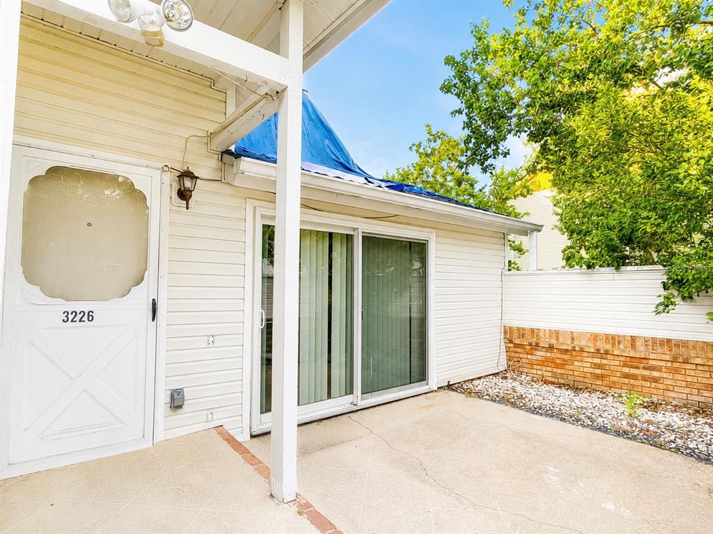 A concrete patio sits outside a white house with a sliding glass door and screen door — 3226 RIO GRANDE TRL UNIT 3226, KISSIMMEE, FL