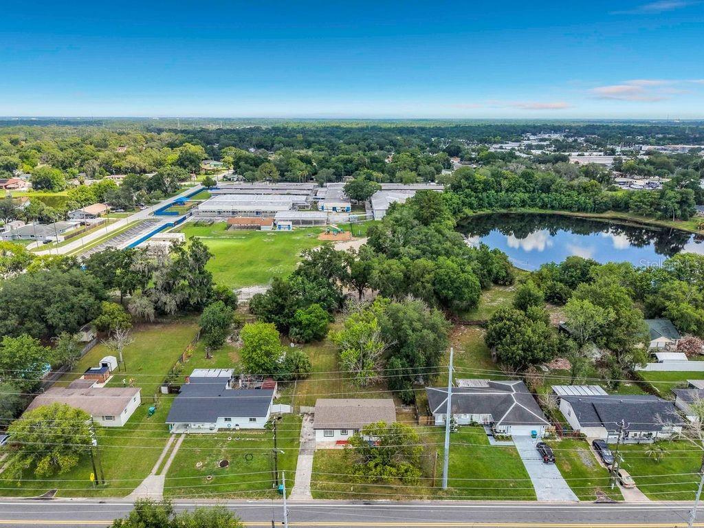 An aerial view shows a residential street with houses, a large grassy field, and a pond — 825 E CHURCH AVE, LONGWOOD, FL
