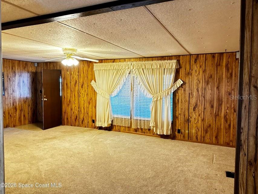 A living room features wood-paneled walls, beige carpeting, a ceiling fan, and draped windows — 4175 HESS AVENUE, COCOA, FL