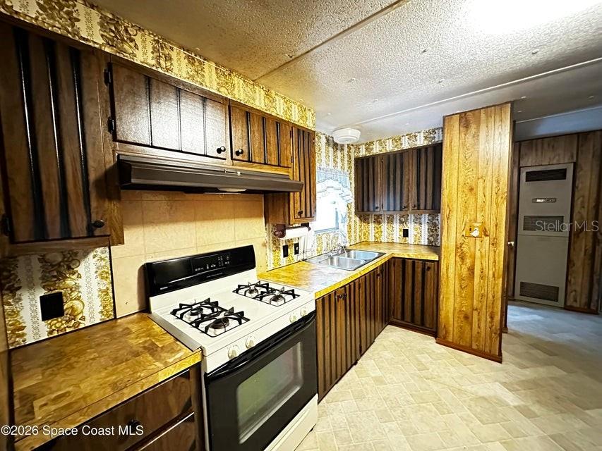 A kitchen features wood-paneled cabinets, patterned wallpaper, a white stove, and laminate countertops — 4175 HESS AVENUE, COCOA, FL