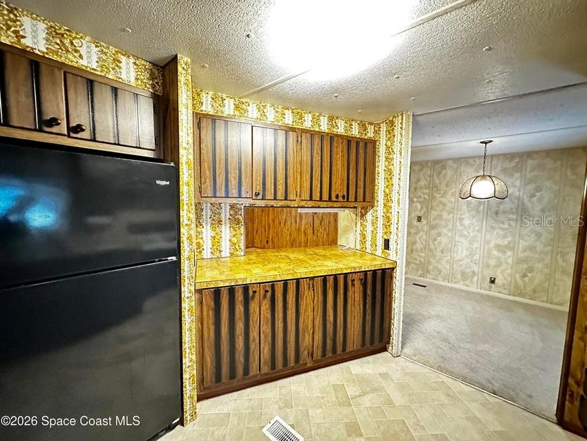 A kitchen features wood-paneled cabinets, yellow patterned wallpaper, and a black refrigerator — 4175 HESS AVENUE, COCOA, FL