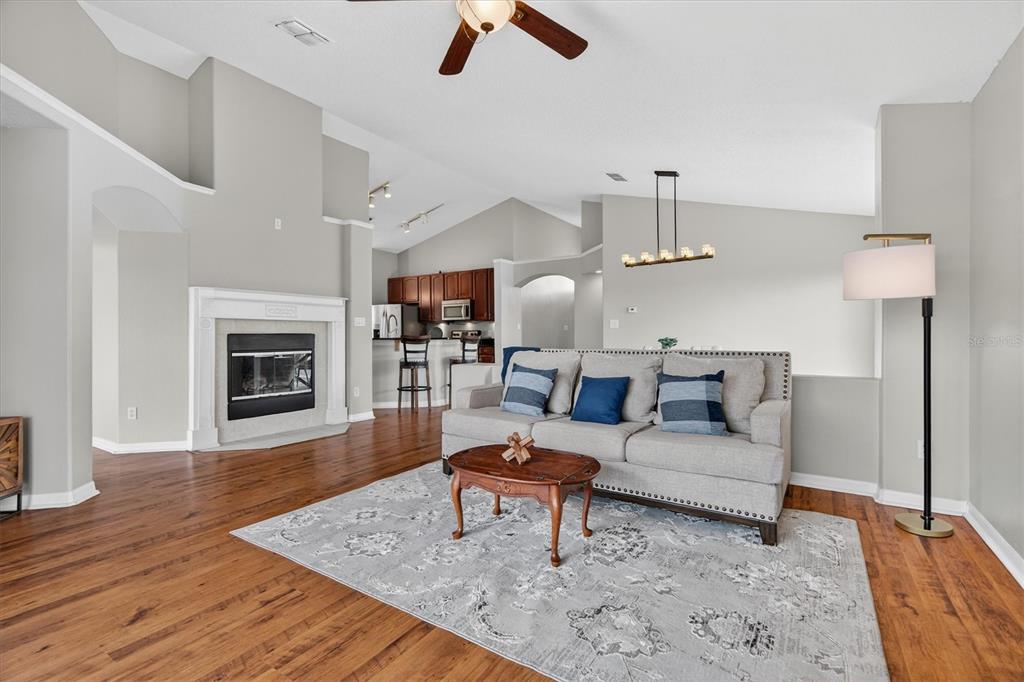 A living room with wood floors, a fireplace, and a sofa facing a kitchen area — 19500 GLEN ELM WAY, ORLANDO, FL
