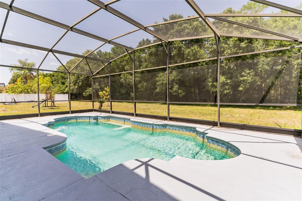 A screened-in swimming pool sits on a concrete patio overlooking a grassy backyard and trees — 2433 HURON CIRCLE, KISSIMMEE, FL