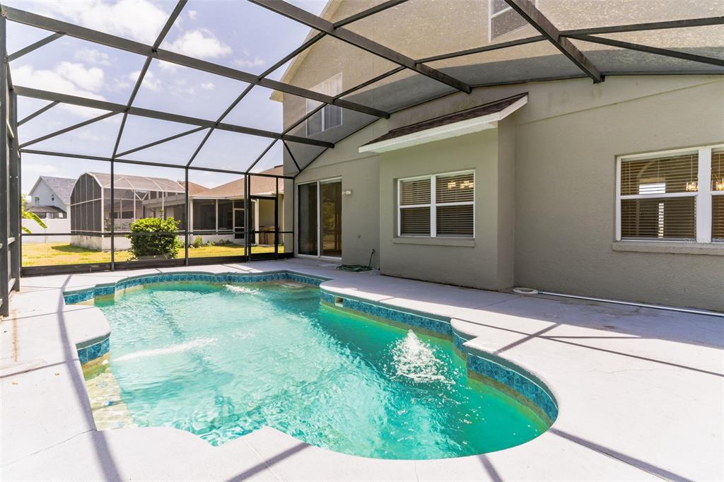A swimming pool with a fountain sits inside a screened-in patio behind a house — 2433 HURON CIRCLE, KISSIMMEE, FL