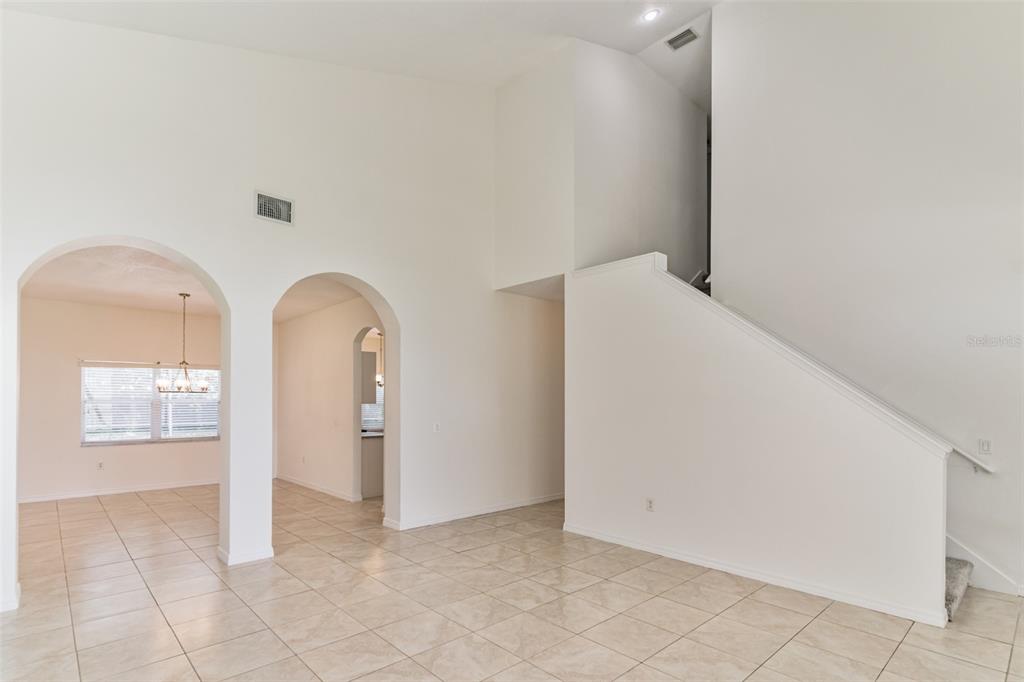 A bright, empty room with tile flooring, arched doorways, and a staircase leading upstairs — 2433 HURON CIRCLE, KISSIMMEE, FL