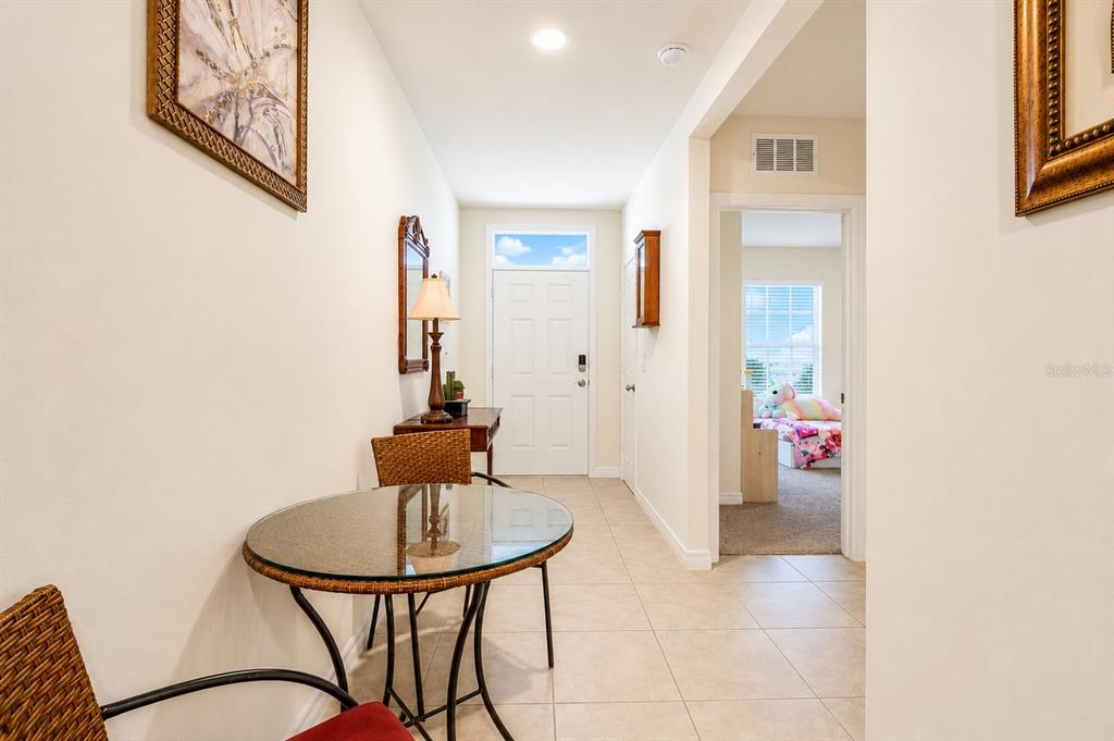 A tiled entryway features a small glass table, wicker chairs, and a view into a bedroom — 3221 CARPENTARIA DRIVE, NEW SMYRNA BEACH, FL