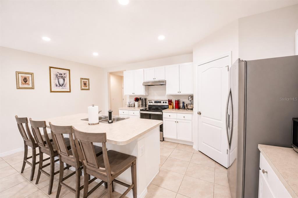 A kitchen features white cabinets, a central island with bar seating, and stainless steel appliances — 3221 CARPENTARIA DRIVE, NEW SMYRNA BEACH, FL