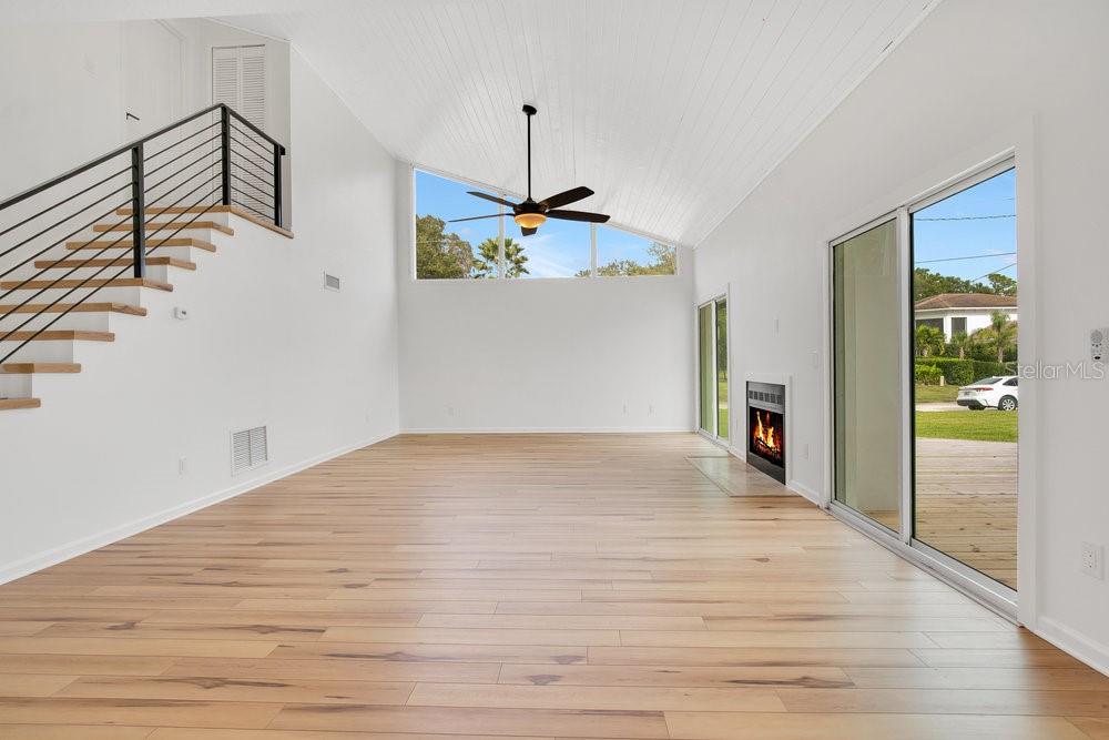 A bright living room features light wood flooring, a vaulted ceiling, a fireplace, and stairs — 905 MAIN STREET, WINDERMERE, FL