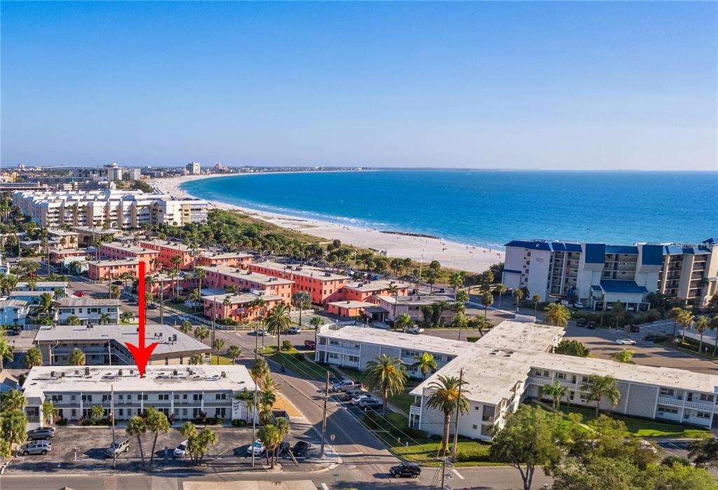 An aerial view shows a multi-story apartment complex near a sandy beach and ocean — 680 71ST AVENUE UNIT 8, ST PETE BEACH, FL