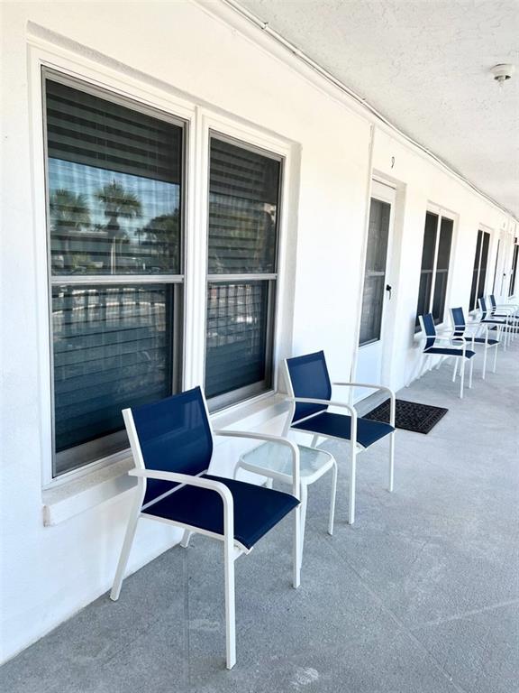 A white exterior walkway features several blue patio chairs and small tables outside windowed units — 680 71ST AVENUE UNIT 8, ST PETE BEACH, FL
