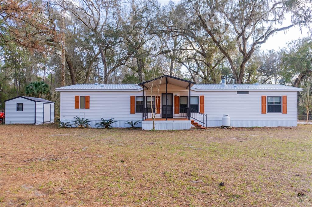 A single-story manufactured home with a metal roof, front porch, and detached shed — 1154 SE 95TH STREET, OCALA, FL