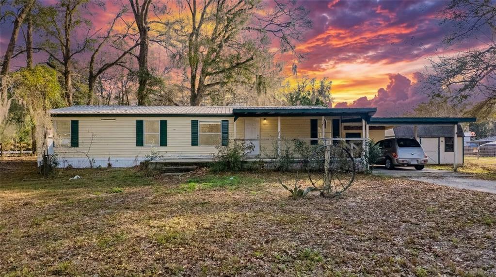 A single-story mobile home with a front porch and attached carport sits under a sunset — 1154 SE 95TH STREET, OCALA, FL