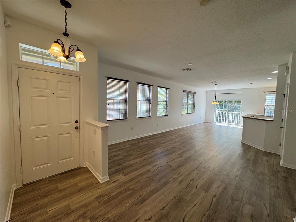 An open-concept living area features wood-look flooring, white walls, and a front entryway — 9124 MOONLIT MEADOWS LOOP, RIVERVIEW, FL
