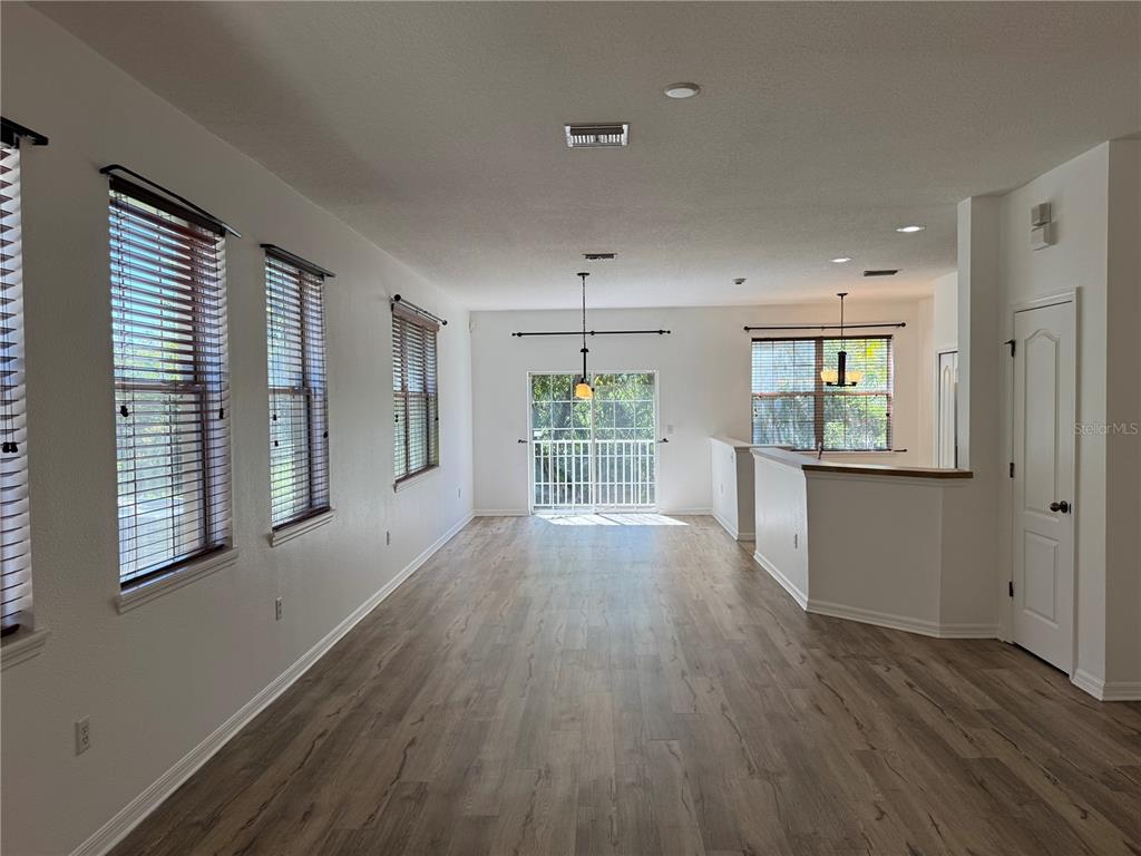 An open-concept living area features wood-look flooring, white walls, and large windows with blinds — 9124 MOONLIT MEADOWS LOOP, RIVERVIEW, FL