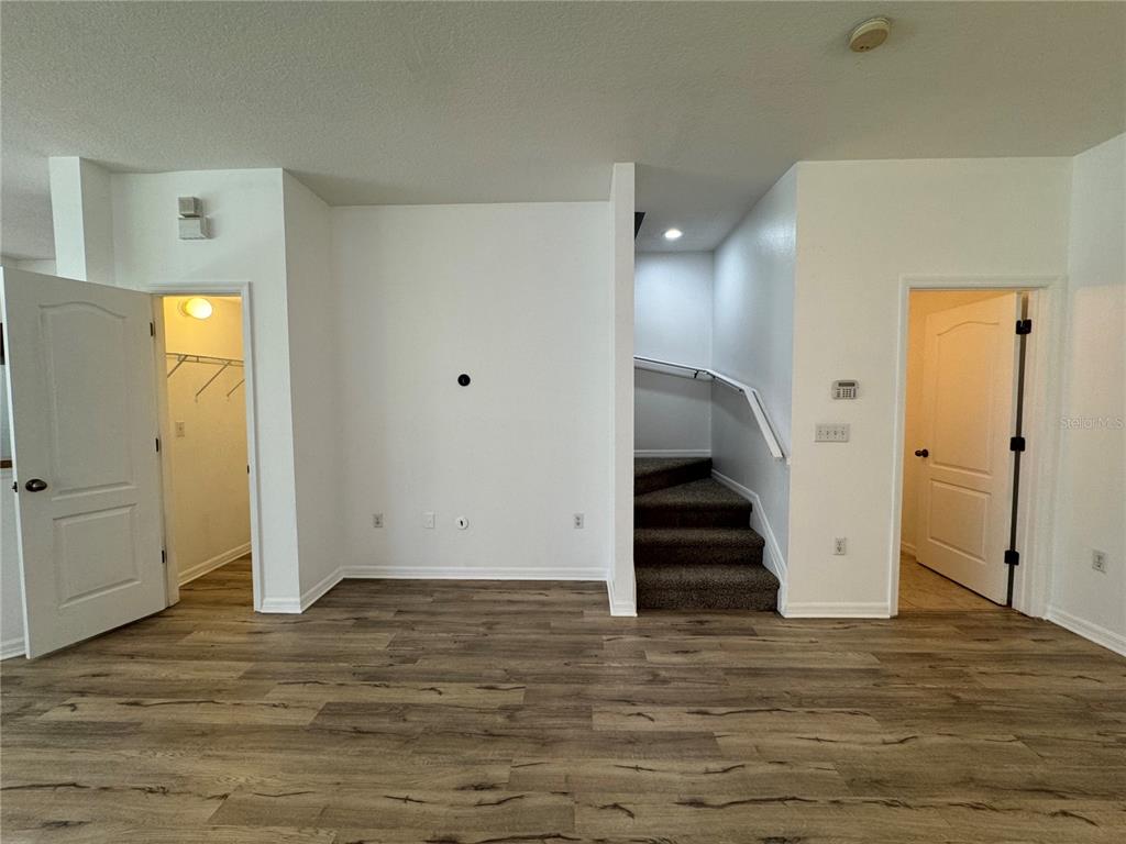 A room with wood-look flooring, a central wall, a staircase, and two open doorways — 9124 MOONLIT MEADOWS LOOP, RIVERVIEW, FL