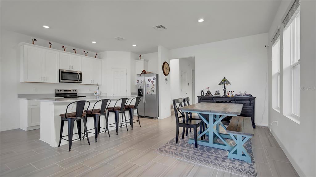A kitchen with white cabinets and an island opens into a dining area with seating — 4704 HOMESTEAD TRAIL, ST CLOUD, FL