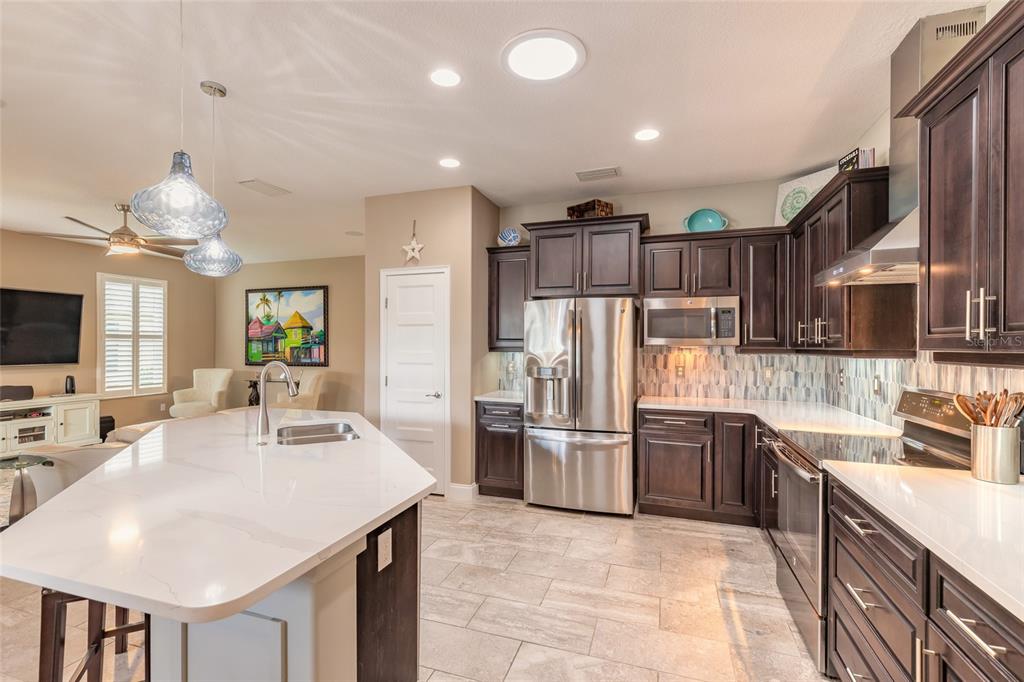 A kitchen with dark wood cabinets, stainless steel appliances, and a white quartz island countertop — 3659 CESI AVENUE, NEW SMYRNA BEACH, FL