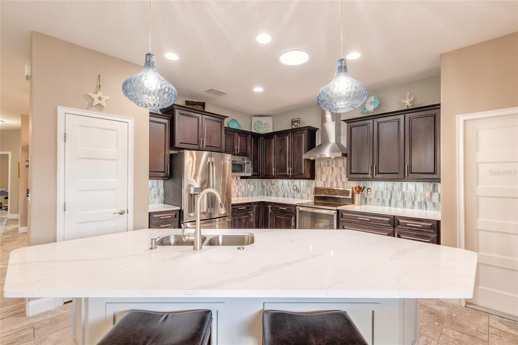 A kitchen features dark wood cabinets, a white quartz island, and blue glass pendant lights — 3659 CESI AVENUE, NEW SMYRNA BEACH, FL