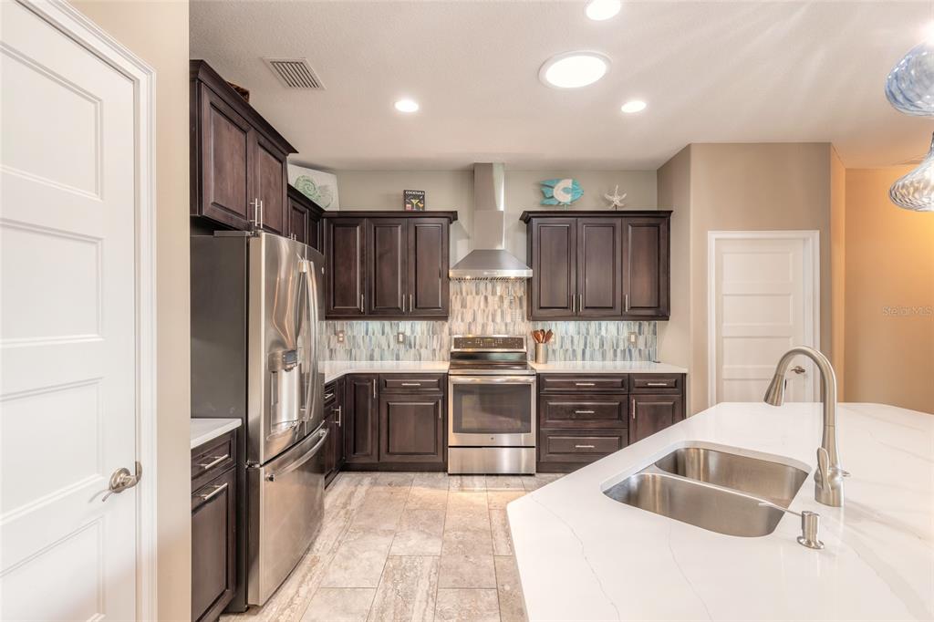 A kitchen features dark wood cabinets, stainless steel appliances, a white island, and tiled flooring — 3659 CESI AVENUE, NEW SMYRNA BEACH, FL