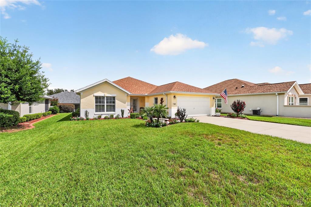 A single-story yellow house with a two-car garage and a green lawn — 11985 SE 91ST CIRCLE, SUMMERFIELD, FL