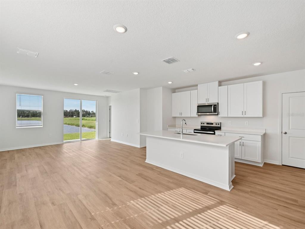A bright, open-concept kitchen and living area featuring white cabinets, an island, and wood flooring — 11267 BELLEWOOD TERRACE, PARRISH, FL