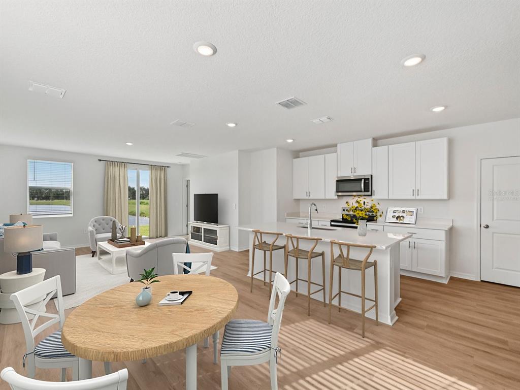 This rendering shows an open-concept kitchen and living area with white cabinets and wood flooring — 11267 BELLEWOOD TERRACE, PARRISH, FL