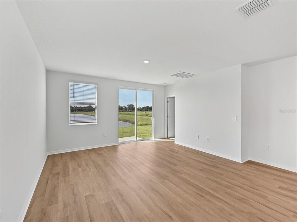An empty room with light wood-look flooring, white walls, and a sliding glass door view — 11267 BELLEWOOD TERRACE, PARRISH, FL