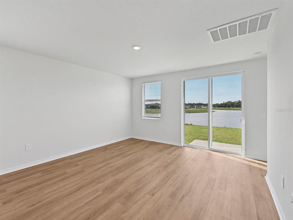 An empty room with light wood-look flooring, white walls, a sliding glass door, and water views — 11267 BELLEWOOD TERRACE, PARRISH, FL