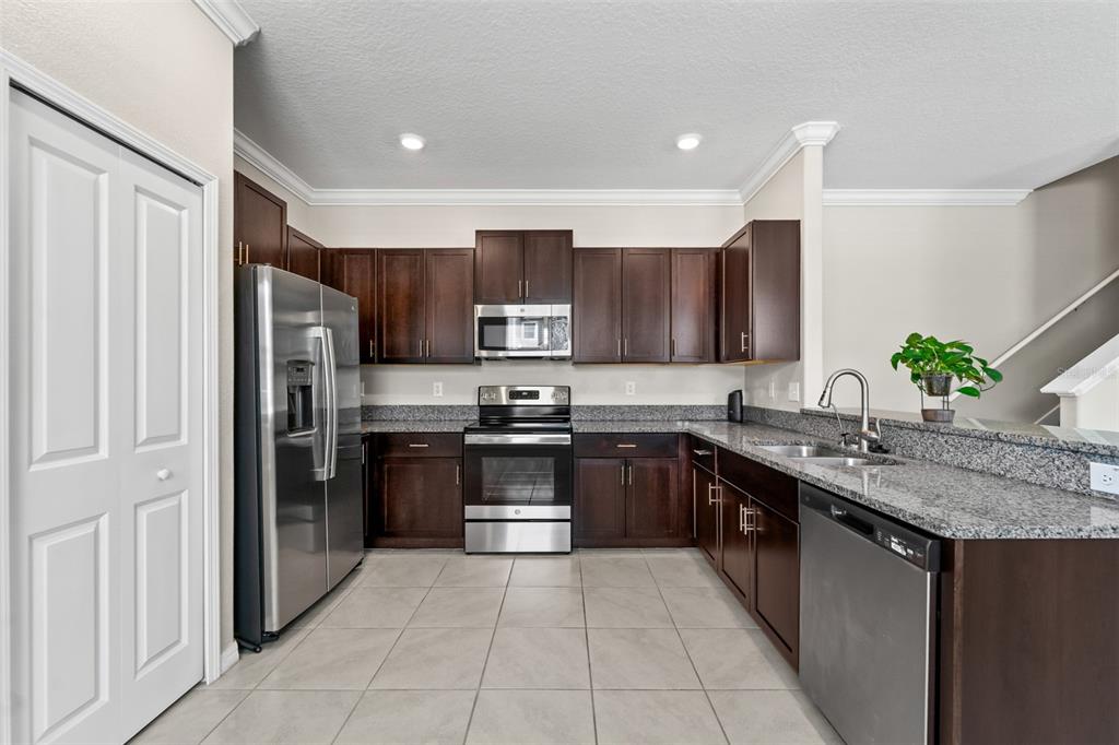 A kitchen with dark wood cabinets, granite countertops, stainless steel appliances, and light tile flooring — 2188 CERULEAN SKY DRIVE, LUTZ, FL