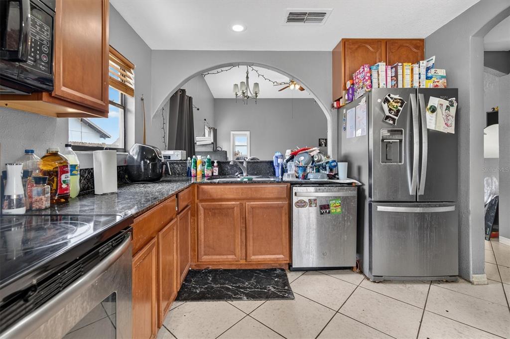 A kitchen features wood cabinets, dark countertops, stainless steel appliances, and an arched opening to another room — 20644 MACON PARKWAY, ORLANDO, FL