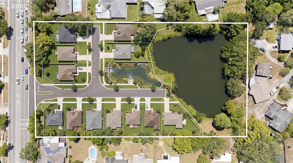An aerial view shows a residential neighborhood with houses surrounding a pond and a fountain — 1276 S BELCHER ROAD, CLEARWATER, FL