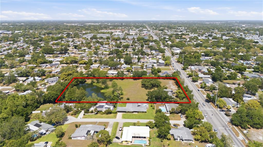 An aerial view shows a vacant, rectangular lot with a pond next to a road — 1276 S BELCHER ROAD, CLEARWATER, FL