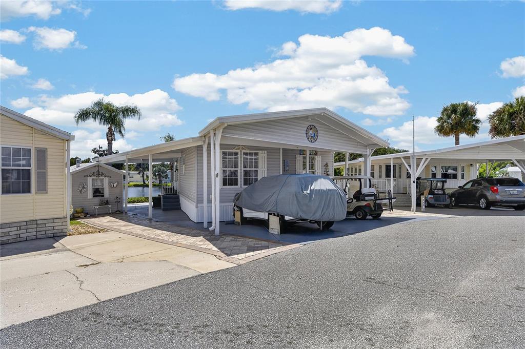 A light-colored manufactured home features a covered carport, a paved driveway, and a golf cart — 370 CITRUS RIDGE DRIVE, DAVENPORT, FL