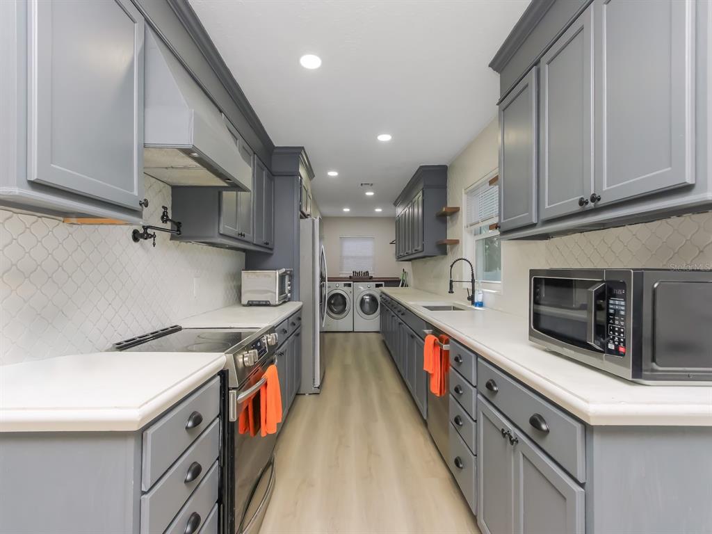A galley-style kitchen features gray cabinets, white countertops, a tile backsplash, and stainless steel appliances — 2011 NANCY ANN TERRACE, OCOEE, FL