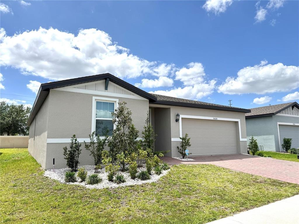 A single-story house with a beige stucco exterior, a two-car garage, and a landscaped front yard — 3024 CASSIDY LANE, HAINES CITY, FL