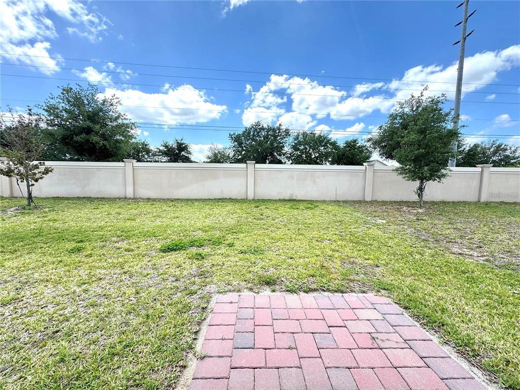 A backyard features a small brick patio, a grassy lawn, and a tall perimeter wall — 3024 CASSIDY LANE, HAINES CITY, FL
