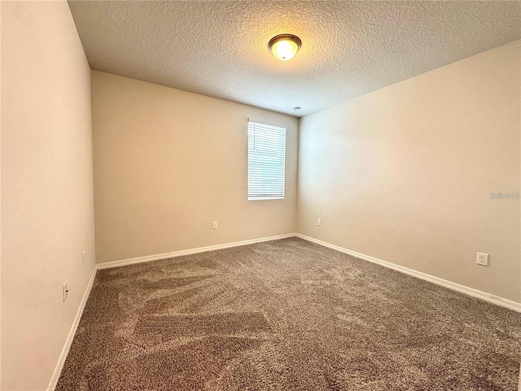 An empty bedroom features beige walls, brown carpet, and a single window with white blinds — 3024 CASSIDY LANE, HAINES CITY, FL