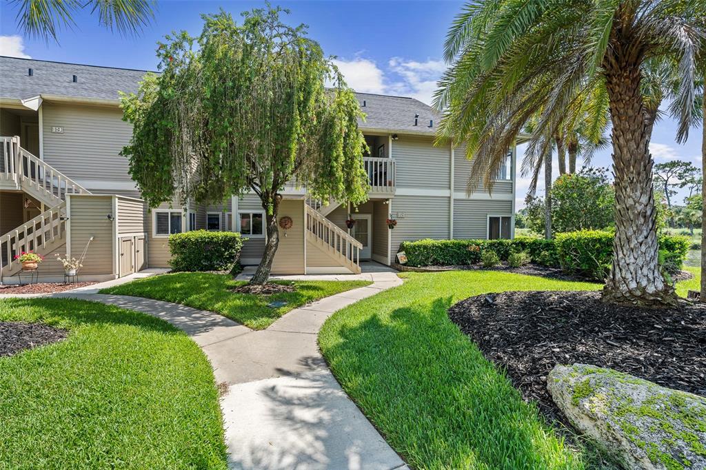 A two-story apartment building with beige siding, outdoor staircases, and a landscaped front yard — 18 MAGNOLIA DRIVE S UNIT B, ORMOND BEACH, FL