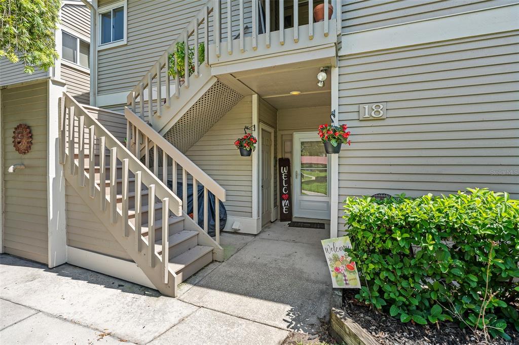 An exterior view of a residential building entrance featuring stairs, a welcome sign, and landscaping — 18 MAGNOLIA DRIVE S UNIT B, ORMOND BEACH, FL