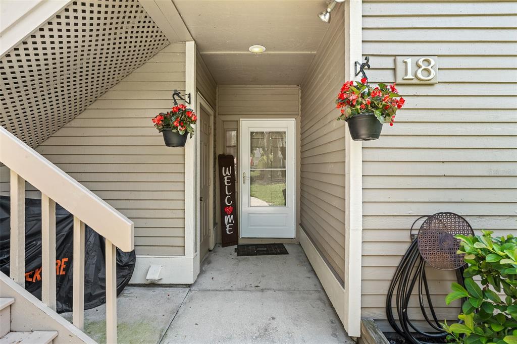 The exterior entryway of a residence features a white door, hanging flower baskets, and stairs — 18 MAGNOLIA DRIVE S UNIT B, ORMOND BEACH, FL